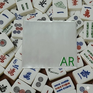 May include: A selection of white Mahjong tiles, each bearing different symbols and Chinese characters, surrounding a clear plastic sleeve. The letters "AR" are visible in green on the sleeve. The tiles have red, blue, and green markings.