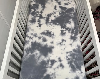 May include: A white and gray tie-dye fitted crib sheet. The sheet is made of soft, breathable fabric and is perfect for a baby's nursery.