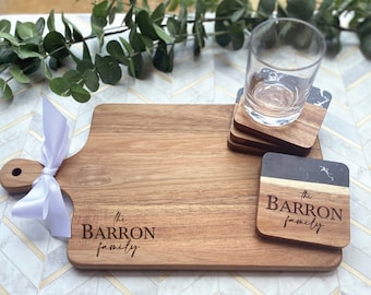 May include: A wooden serving board with a handle and the text "the Barron family" engraved on it.  Four coasters with a black and white marble design are also included, with the text "the Barron family" engraved on one of the coasters.
