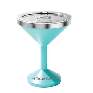 May include: A turquoise martini-shaped tumbler with a clear lid and a silver-toned rim. The base features the text A 'tini bit drunk! with a small martini glass icon. The vessel has a wide bowl, a slender stem, and a circular pedestal base.