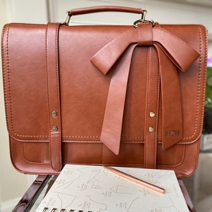 Photo of brown leather laptop briefcase with laser engraved monogram on bow. Professional work laptop bag for woman with monogram. Vegan leather satchel with laptop compartment for woman. Personalized work bag for woman with name or initials on bag.