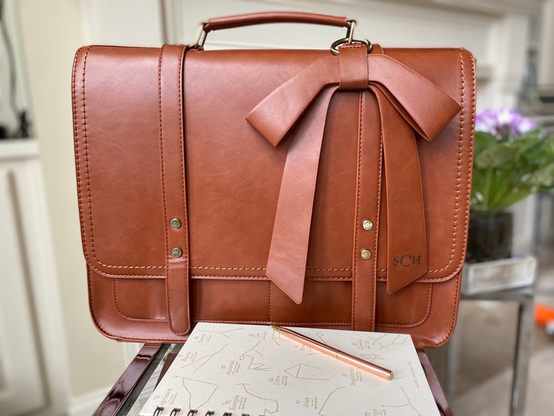 Photo of brown leather laptop briefcase with laser engraved monogram on bow. Professional work laptop bag for woman with monogram. Vegan leather satchel with laptop compartment for woman. Personalized work bag for woman with name or initials on bag.