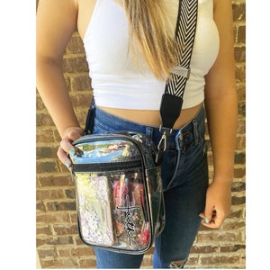 May include: Clear crossbody bag with a black strap and the word "Faith" printed on the front. The bag has a zipper closure and a small pocket on the front.