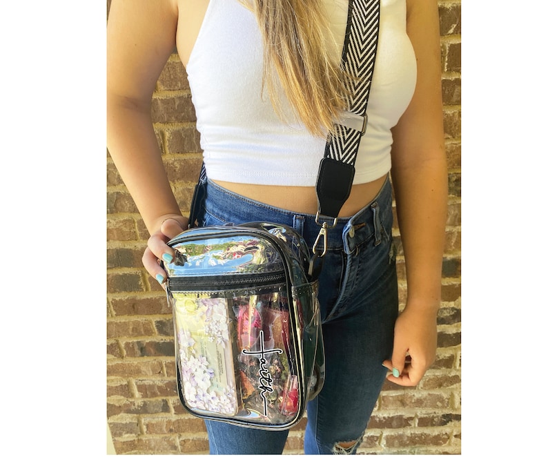 May include: Clear crossbody bag with a black strap and the word "Faith" printed on the front. The bag has a zipper closure and a small pocket on the front.