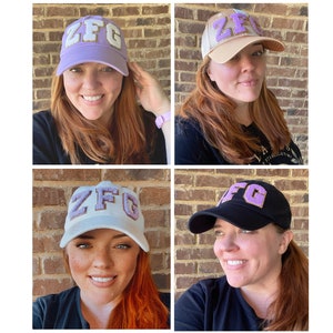 May include: Four different views of a baseball cap with the letters "ZFG" in purple felt on the front of the cap. The caps are in different colors: purple, beige, white, and black.