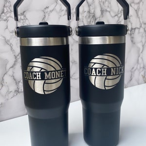 May include: Two black stainless steel travel mugs with handles. The mugs have a volleyball graphic and the text "Coach Monet" and "Coach Nick" engraved on them.