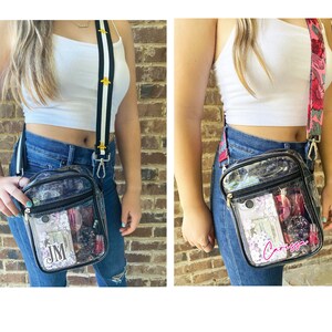 May include: Two clear plastic crossbody bags with black straps. The bag on the left has a black and white striped strap with gold bee accents and the text "JM" inside. The bag on the right has a pink and green floral strap and the text "Carissa" inside.