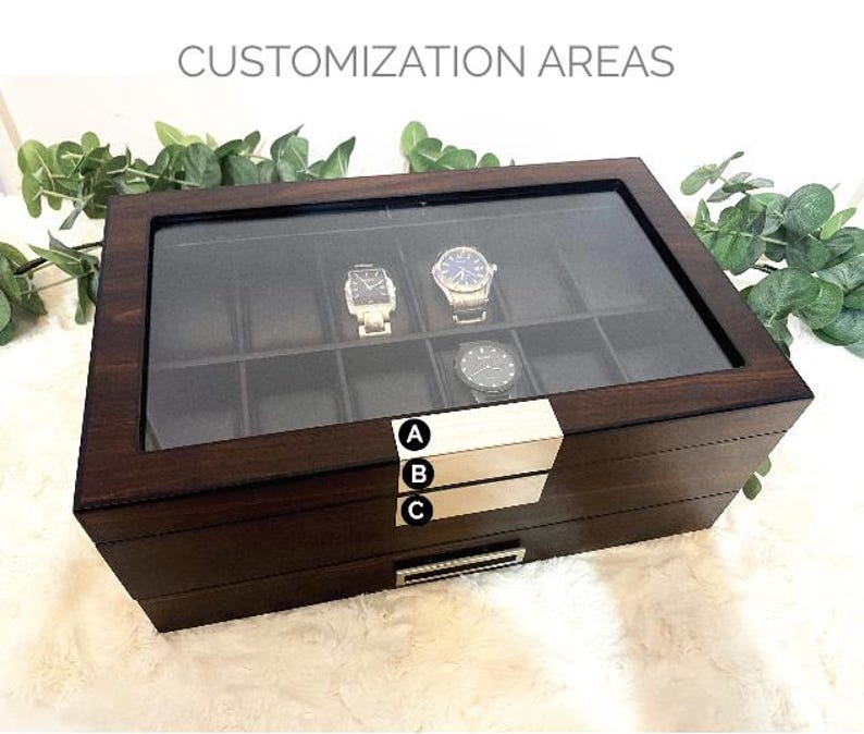 Puede incluir: Una caja para relojes de madera marr&oacute;n oscuro con tapa de cristal y diez compartimentos interiores. El frente presenta dos placas met&aacute;licas plateadas etiquetadas A, B y C para &aacute;reas de personalizaci&oacute;n y un caj&oacute;n inferior con asa.