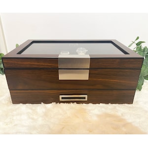Front center view of walnut woodgrain watch display case. This watch box features slots with pillows to store and display 12 watches. Below display compartment is a valet drawer to organize mens accessories like cuff links, tie bars, collar stays