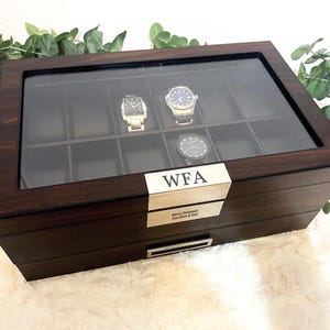 Puede incluir: Una caja de madera de color marr&oacute;n oscuro para relojes con tapa de cristal, que contiene diez compartimentos interiores y tres relojes de pulsera. Una placa met&aacute;lica dorada en el frente est&aacute; grabada con las letras WFA y otra placa dice Merry Christmas Love Mom & Dad.