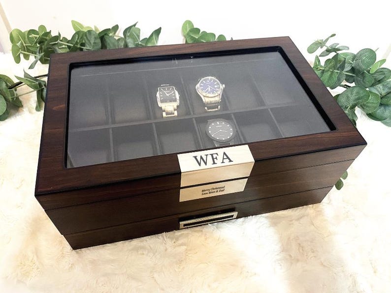 Puede incluir: Una caja de madera de color marr&oacute;n oscuro para relojes con tapa de cristal, que contiene diez compartimentos interiores y tres relojes de pulsera. Una placa met&aacute;lica dorada en el frente est&aacute; grabada con las letras WFA y otra placa dice Merry Christmas Love Mom & Dad.