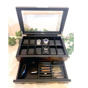 Large mens watch and accessories jewelry box is shown with glass lid and valet drawer open. Watch box has slots for 12 watches. 3 watches are shown in use. Valet tray shows accessories like rings, tie bars, collar stays, cuff links, pocket knife