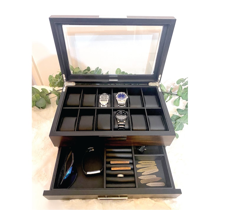 Large mens watch and accessories jewelry box is shown with glass lid and valet drawer open. Watch box has slots for 12 watches. 3 watches are shown in use. Valet tray shows accessories like rings, tie bars, collar stays, cuff links, pocket knife
