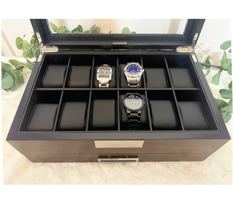 Walnut finished wood watch display case with black faux leather interior and watch pillows. Watch box case is displayed with glass lid open.