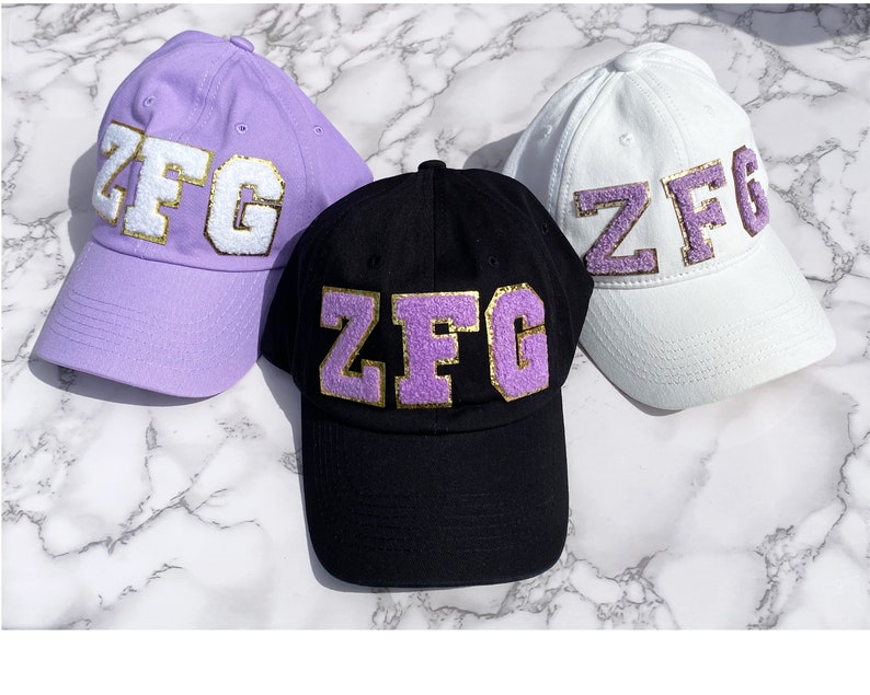 Custom cotton baseball hat for women with varsity letters. Chenille and glitter letters on lavender baseball hat for women, black baseball cap for her and white ball cap for woman. Varsity letter patch in white with gold trim and lavender with gold
