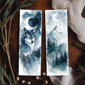 May include: Two watercolor bookmarks. One features a wolf with a crescent moon, the other a wolf on a mountain. Both have a dark blue and gray color scheme with forest and mountain imagery.