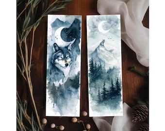 Puede incluir: Dos marcapáginas de acuarela. Uno presenta un lobo con una luna creciente, el otro un lobo en una montaña. Ambos tienen una combinación de colores azul oscuro y gris con imágenes de bosques y montañas.