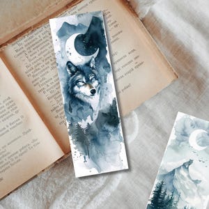 May include: Watercolor bookmarks featuring a wolf, mountains, and a crescent moon. The bookmarks have a blue and gray color scheme with a forest scene. The artwork is on a white background.