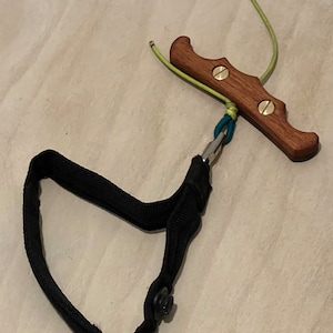 May include: A wooden handle with two brass screws and a green cord attached to a black strap with a metal clip.