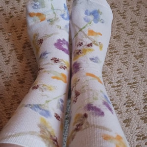 May include: A pair of white socks with a floral pattern in shades of blue, yellow, orange, and purple.