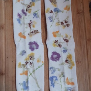 May include: A pair of white socks with a floral print. The socks feature a variety of flowers in shades of blue, yellow, orange, and purple.