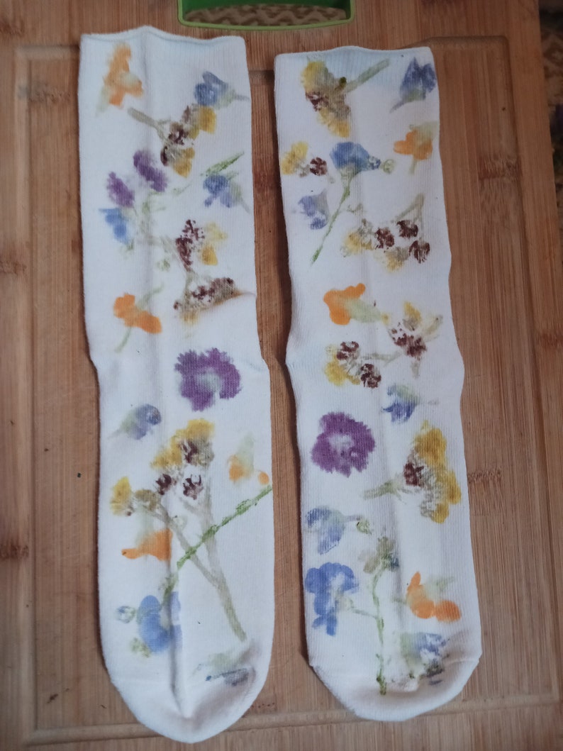 May include: A pair of white socks with a floral print. The socks feature a variety of flowers in shades of blue, yellow, orange, and purple.