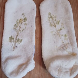 May include: Two white socks with a green plant design printed on them. The socks are lying on a wooden surface.