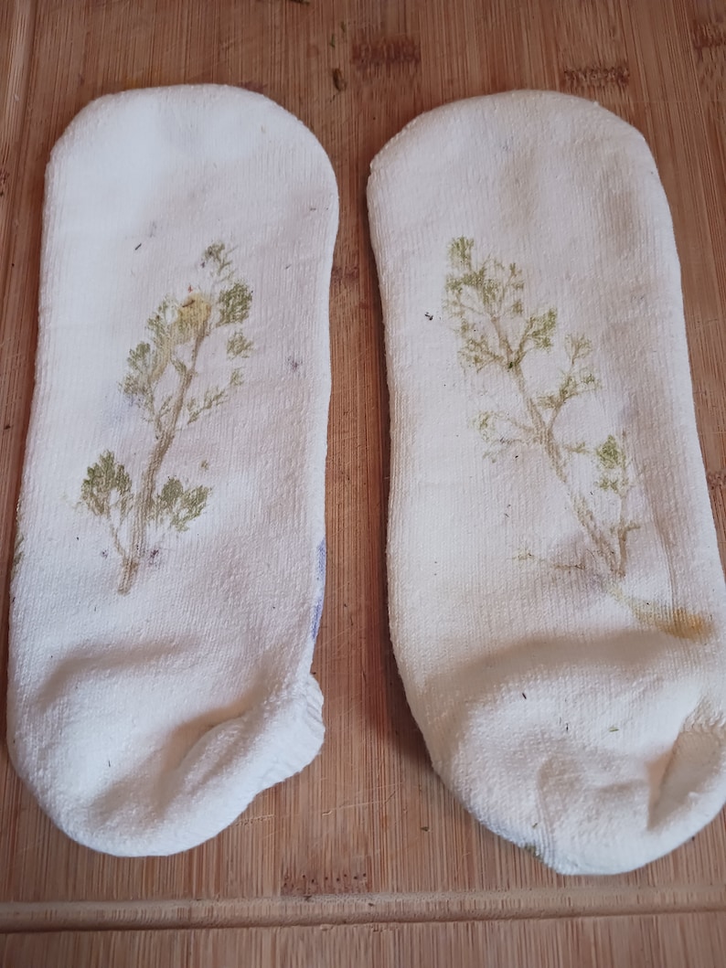 May include: Two white socks with a green plant design printed on them. The socks are lying on a wooden surface.
