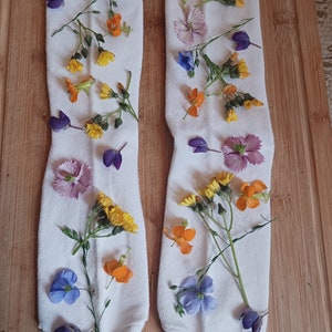 May include: Two white socks with pressed flowers in various colors, including purple, blue, yellow, and orange.