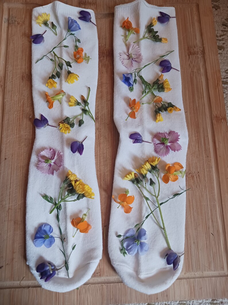 May include: Two white socks with pressed flowers in various colors, including purple, blue, yellow, and orange.