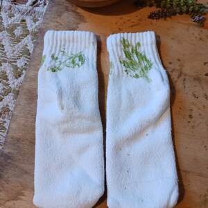 May include: A pair of white socks with green leaf prints. The socks are made of a soft, comfortable material.