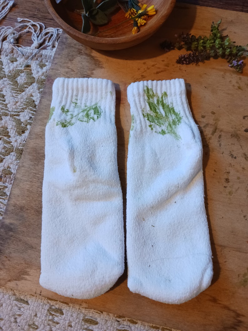 May include: A pair of white socks with green leaf prints. The socks are made of a soft, comfortable material.
