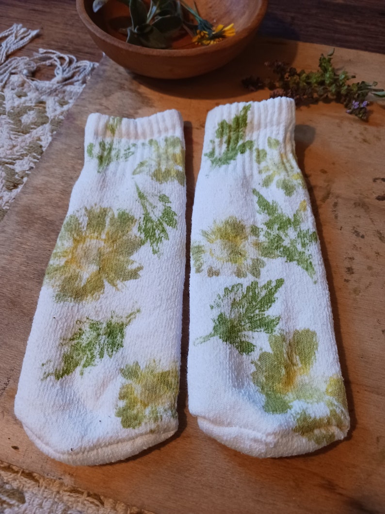 May include: A pair of white socks with a floral print in shades of green and yellow.