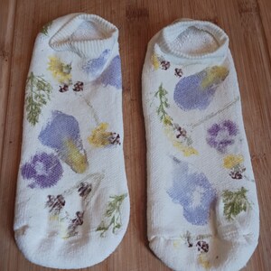 May include: A pair of white socks with a floral design. The socks have a variety of purple, yellow, and brown flowers printed on them.