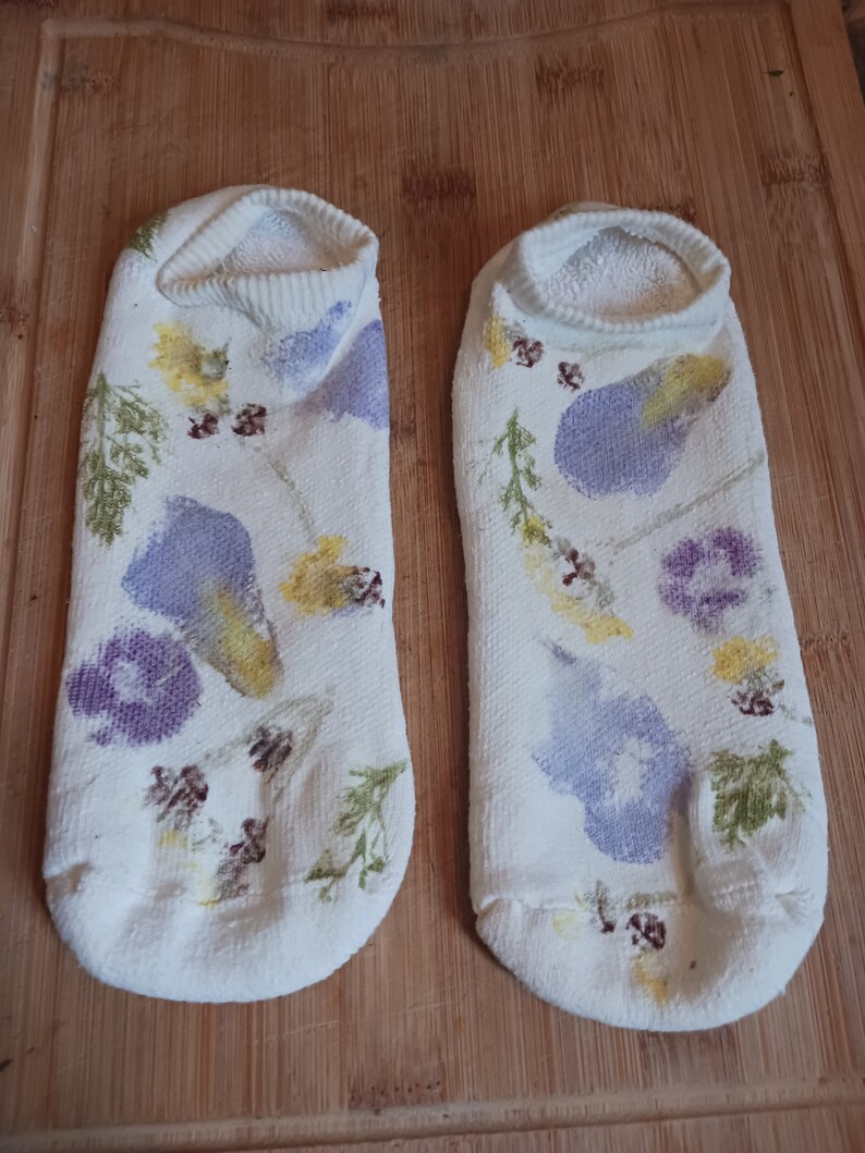 May include: A pair of white socks with a floral design. The socks have a variety of purple, yellow, and brown flowers printed on them.