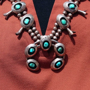 May include: A silver and turquoise necklace with a crescent moon pendant. The necklace has a beaded chain and multiple turquoise stones.