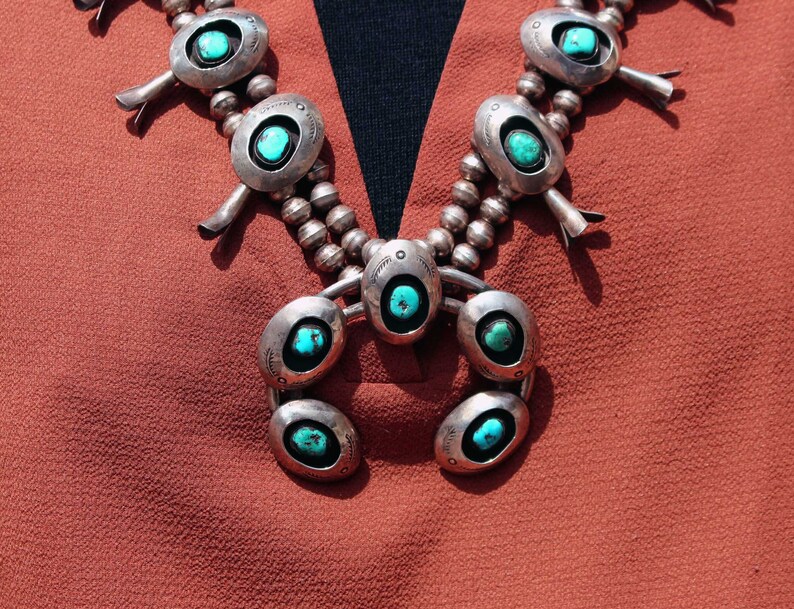 May include: A silver and turquoise necklace with a crescent moon pendant. The necklace has a beaded chain and multiple turquoise stones.