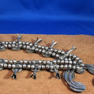 May include: A silver Native American squash blossom necklace with a beaded chain and multiple silver pendants. The necklace is laid out on a brown surface.