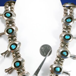 May include: A silver and turquoise necklace with a beaded chain and oval-shaped pendants. Each pendant features a turquoise stone and a silver design. The necklace is displayed on a white mannequin.