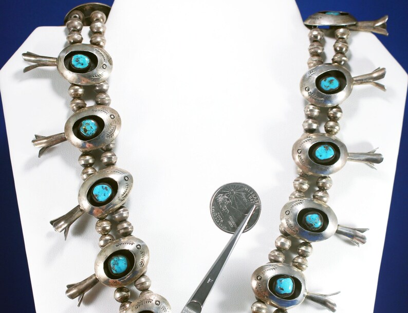 May include: A silver and turquoise necklace with a beaded chain and oval-shaped pendants. Each pendant features a turquoise stone and a silver design. The necklace is displayed on a white mannequin.