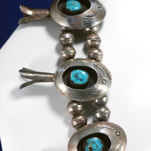 May include: A silver necklace featuring turquoise stones and silver beads. The necklace has a distinctive design with a silver pendant that incorporates a turquoise stone at its centre.