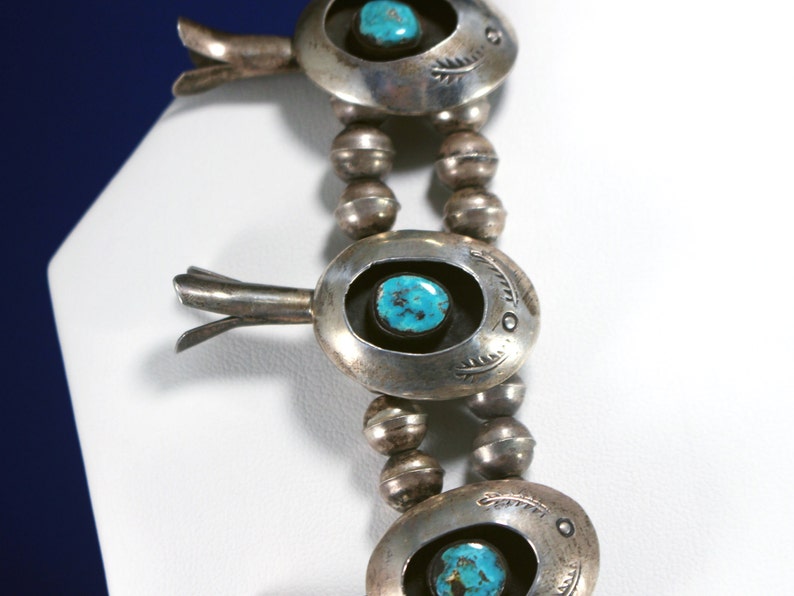 May include: A silver necklace featuring turquoise stones and silver beads. The necklace has a distinctive design with a silver pendant that incorporates a turquoise stone at its centre.
