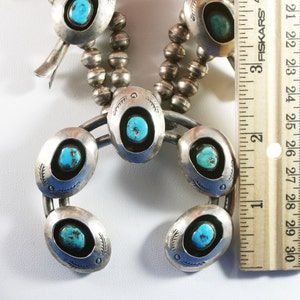 May include: A silver and turquoise necklace with a horseshoe pendant. The pendant has five turquoise stones set in silver. The necklace is 28 inches (71 cm) long.