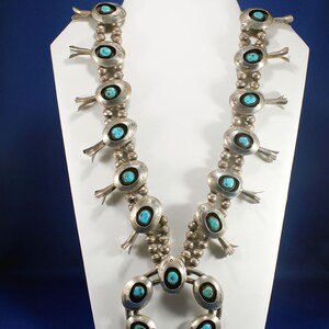 May include: A silver and turquoise Native American necklace with a horseshoe pendant. The necklace features multiple turquoise stones set in silver, and the pendant has a turquoise stone in the centre.