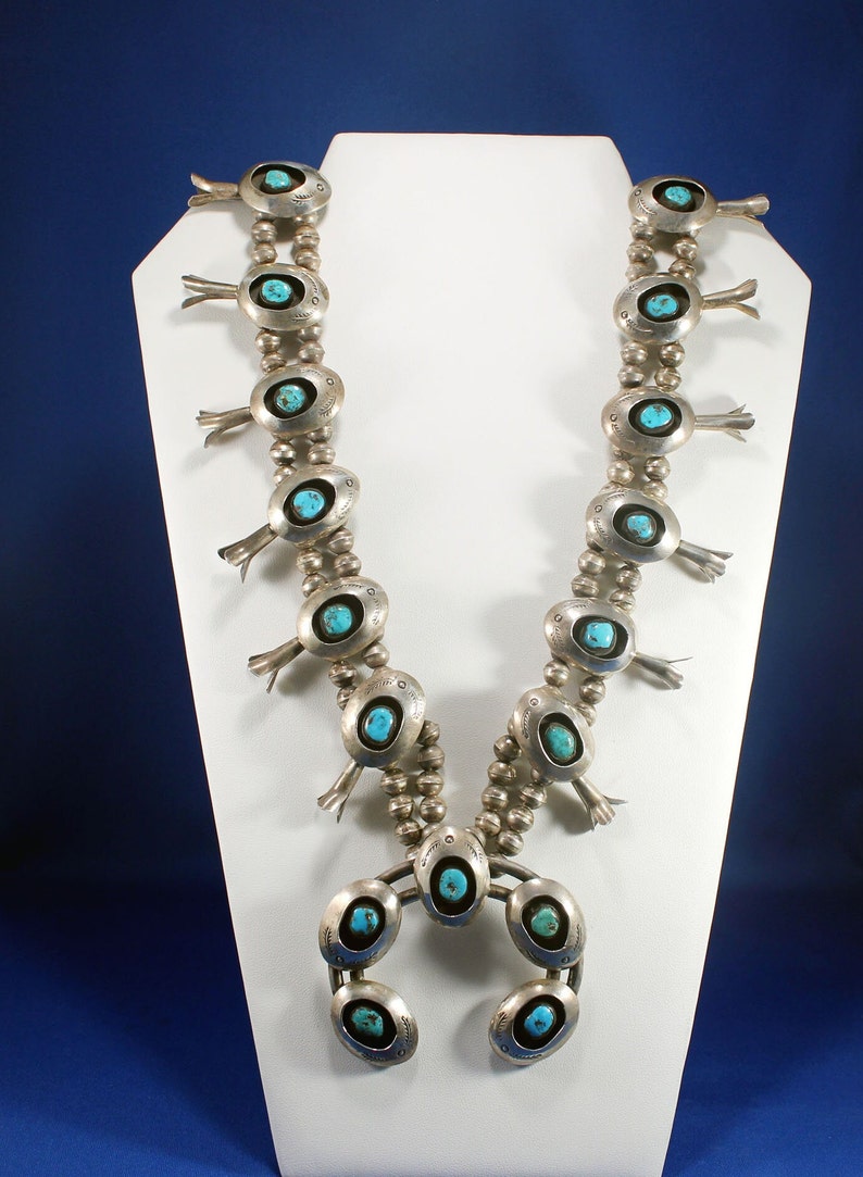 May include: A silver and turquoise Native American necklace with a horseshoe pendant. The necklace features multiple turquoise stones set in silver, and the pendant has a turquoise stone in the centre.