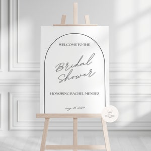 May include: A white sign with a black archway design. The text reads "Welcome to the Bridal Shower Honoring Rachel Mendez May 16, 2024".