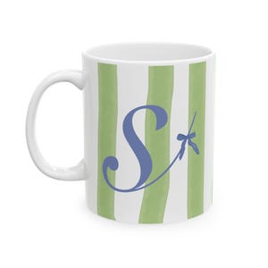 Pode incluir: Caneca de cerâmica branca com listras verdes e brancas. A caneca tem uma letra "S" azul com uma libélula azul em uma listra verde.