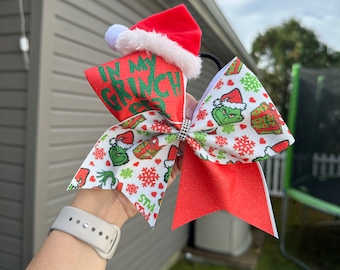 May include: A white and green Grinch-themed hair bow with a red glitter bow and a red Santa hat. The bow has a white background with green snowflakes, hearts, and Grinch faces. The text "In My Grinch Gear" is on the bow.