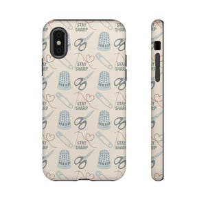 May include: A phone case with a repeating pattern of sewing tools. The design includes scissors, thimbles, safety pins, and thread hearts, with the text "STAY SHARP" scattered throughout. The case is light beige.