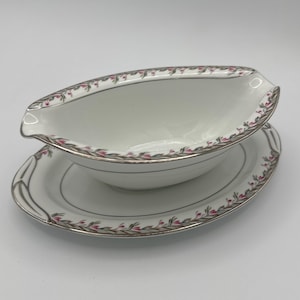 Könnte beinhalten: Eine weiße Porzellansauce mit einem rosa-grünen Blumendesign und goldenen Verzierungen. Die Sauce steht auf einer passenden Untertasse.